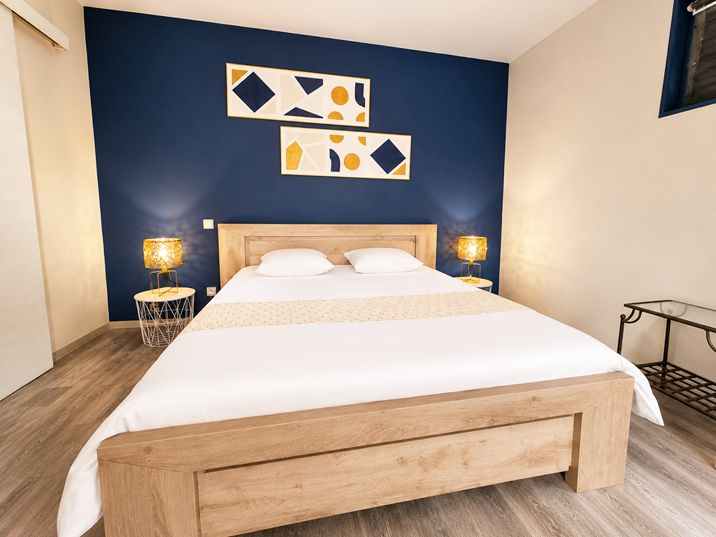 Lit double avec linge blanc, tête de lit en bois et lampes de chevet devant un mur bleu.