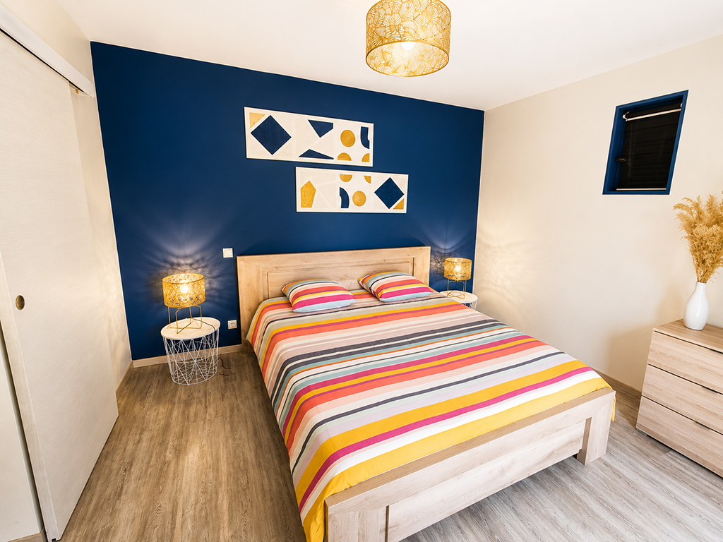 Chambre avec lit double, couvre-lit à rayures multicolores et mur bleu foncé.