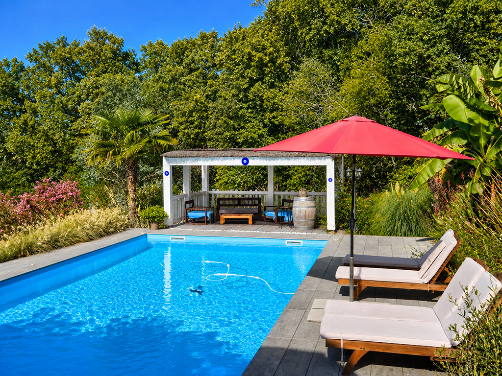 Piscine extérieure entourée de transats, avec parasol rouge et terrasse couverte.