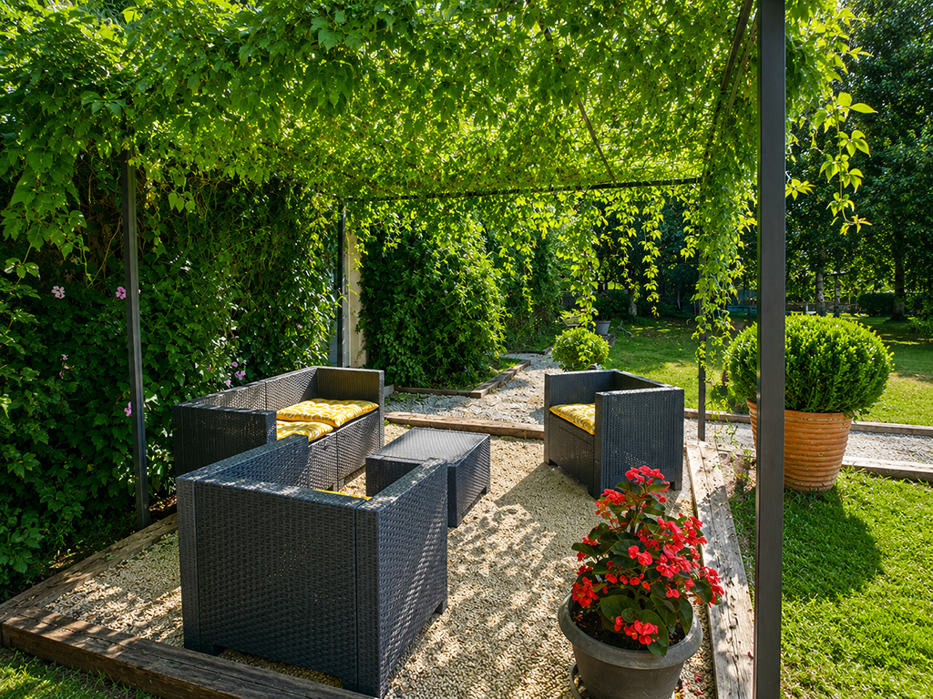Salon de jardin sous une pergola végétalisée, bordé de plantes fleuries.