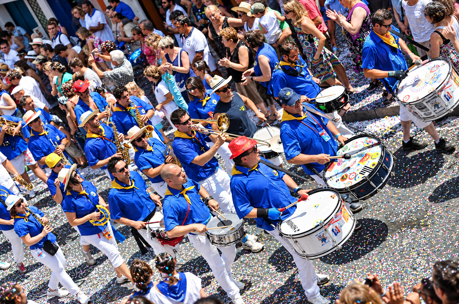 Musiciens d’une banda en chemises bleues et foulards jaunes défilant au milieu du public